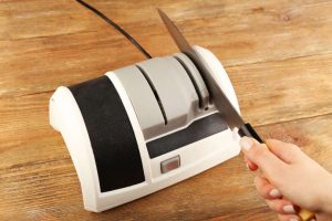 Sharpening knife with electric knife sharpener on wooden background