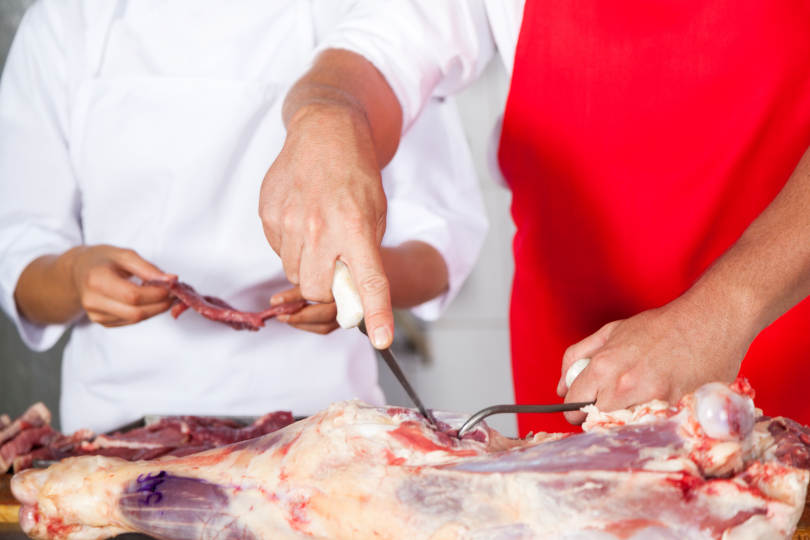 Midsection of butcher cutting meat with boning knife