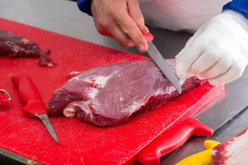 Chef cutting meat with meat cutting knife on a cutting board