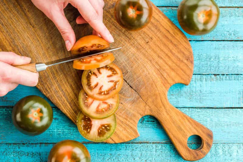 Chef cutting tomato on a cutting board with tomato knife