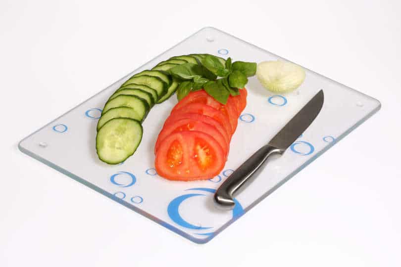 Sliced cucumbers, onions, tomatoes on a glass cutting board