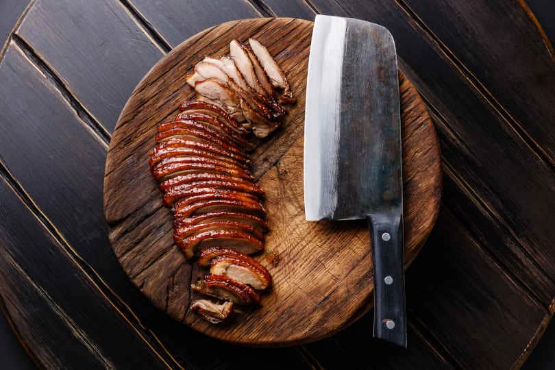 Sliced Peking Duck and Chinese cleaver on cutting board on black wooden background