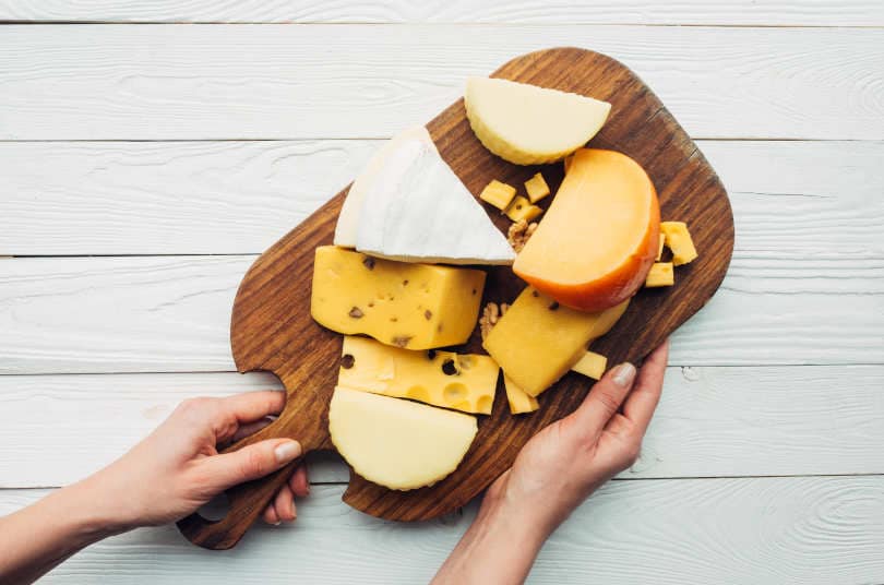 Hands and assorted cheese on wooden cheese board