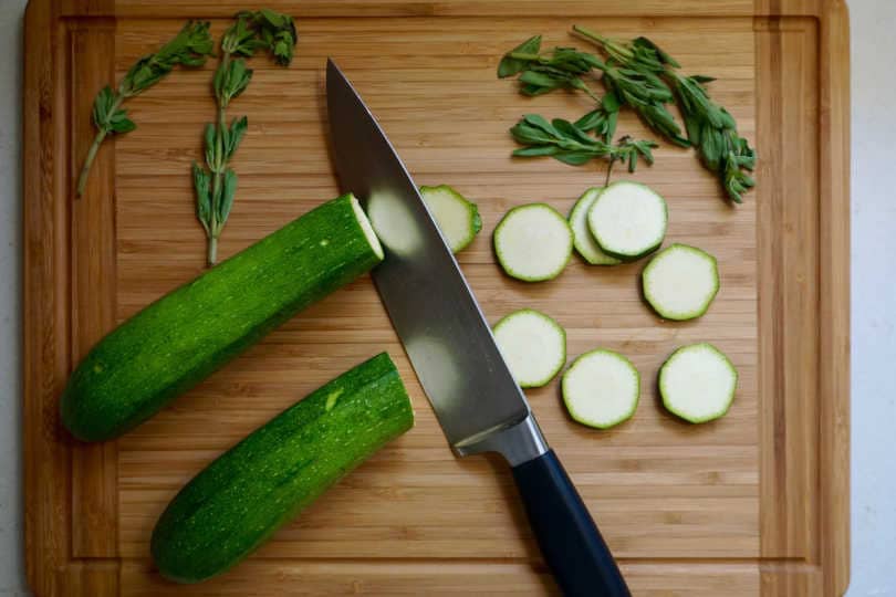 Slicing zucchini and oregano on a bamboo cutting board