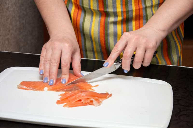 Left-handed girl is slicing salmon into strips on a white board on the black table