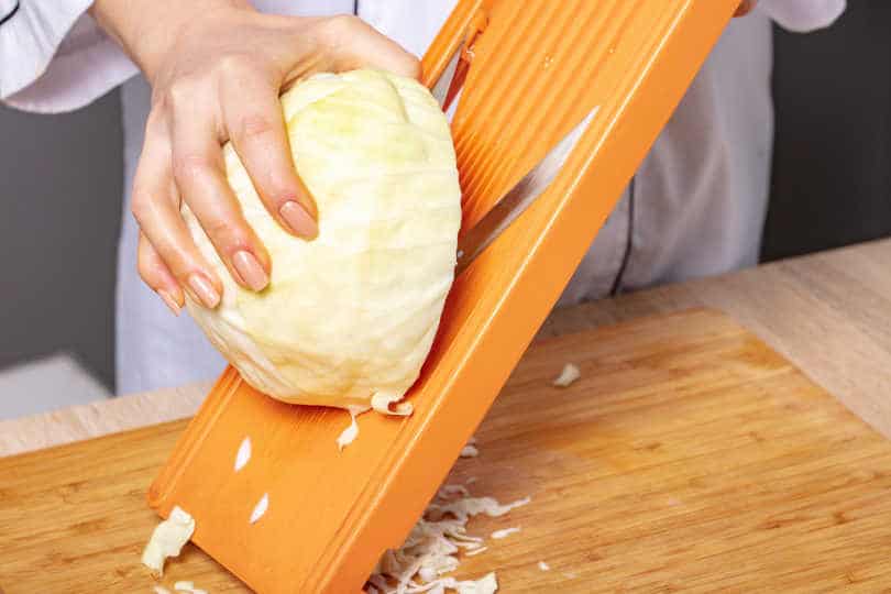 Slicing cabbage on shredder, preparation for cooking