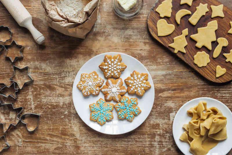 Flat lay with Christmas cookies on plate, ingredients and cookie cutters arranged on wooden tabletop