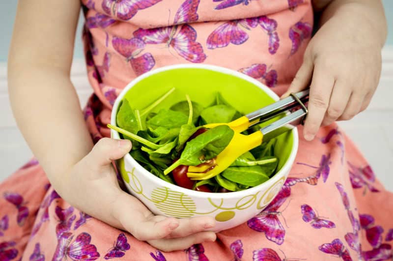 Child taking salad from bowl, using yellow salad tong