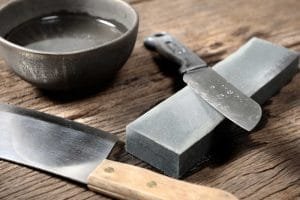 Knives, bowl and whetstone on a board to sharpen knives