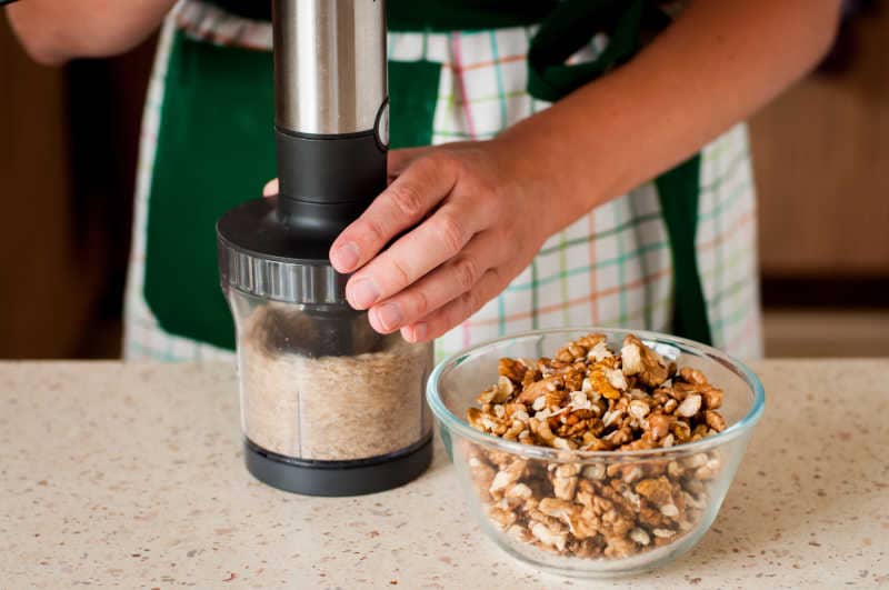 A Woman Wearing Apron Chopping Walnuts in a Nut Chopper