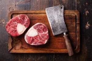 Raw fresh cross cut veal shank and meat cleaver on wooden cutting board