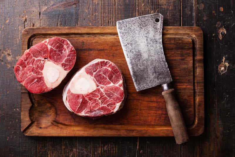 Raw fresh cross cut veal shank and meat cleaver on wooden cutting board