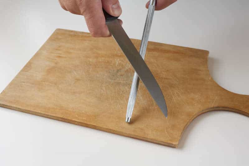 Man hones knife with knife sharpener rod on wooden cutting board