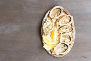 Plate of raw fresh open oysters shells with lemons, top view on wooden table