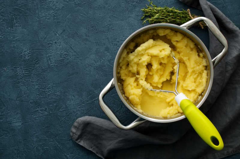 Mashed potatoes in bowl on a dark stone blue table, rosemary, napkin, top view