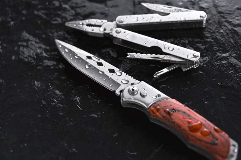 Folding knife and folding pliers on black background