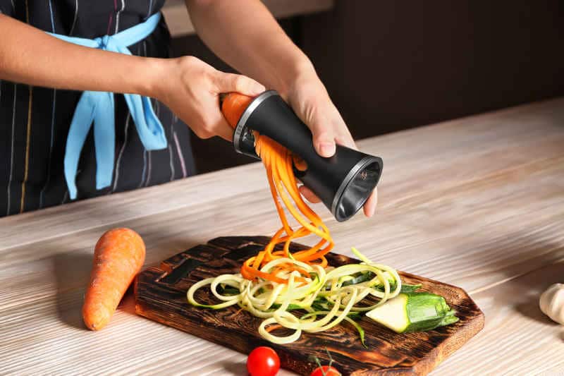 Woman making zucchini and carrot spaghetti with handheld spiralizer