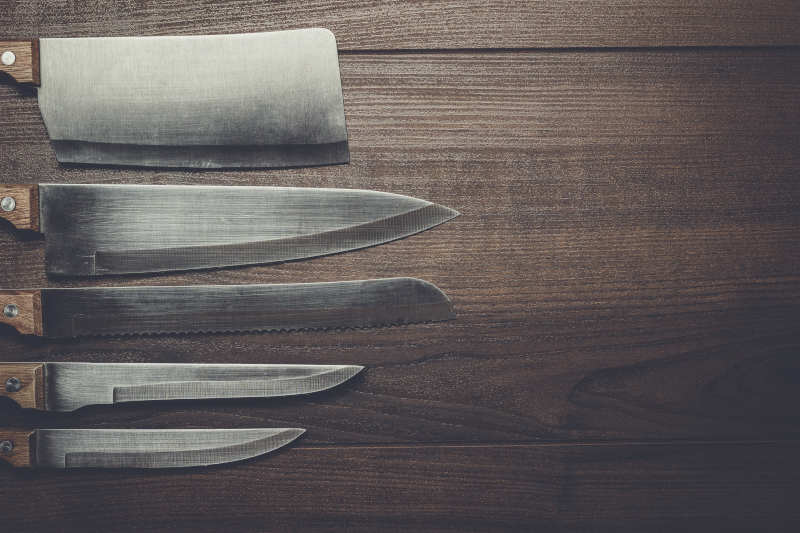 Five kitchen knives on the brown wooden background
