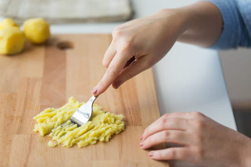 Hand with fork making mashed potato on wooden board