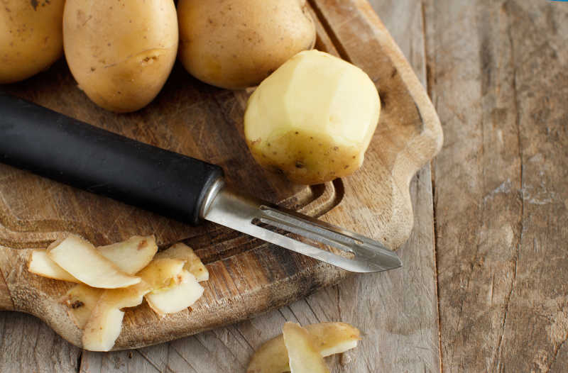 Raw potatoes with a potato peeler on a cutting board