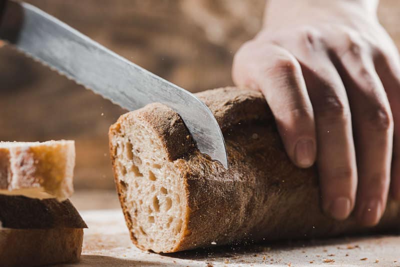 Whole grain bread put on kitchen wood plate with a chef holding bread knife for cut