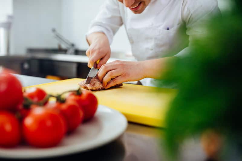 A young male chef cutting the meat in a professional kitchen