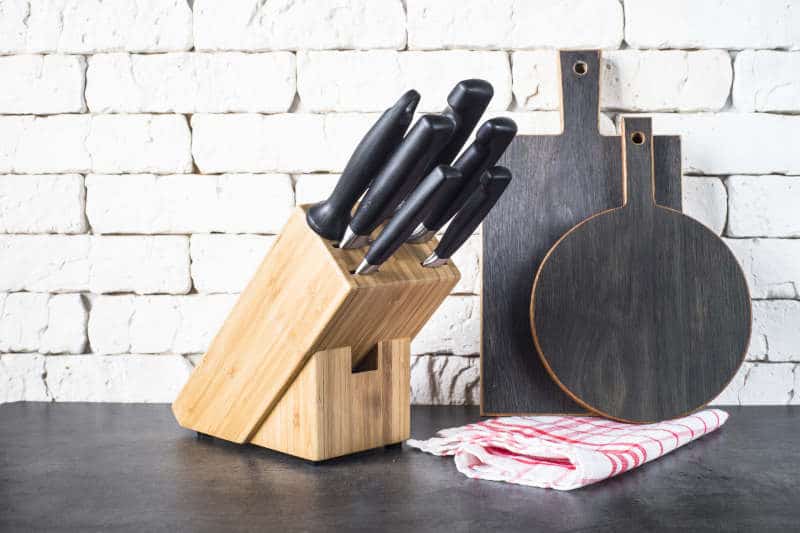 Sel sharpening knives in the wooden block on the grey stone table near the brick wall.