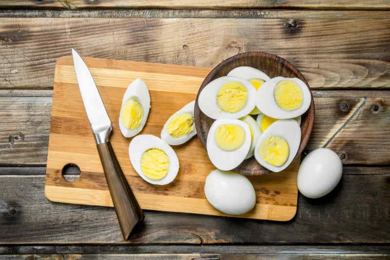 Sliced boiled eggs and a knife on cutting board. On a wooden background.