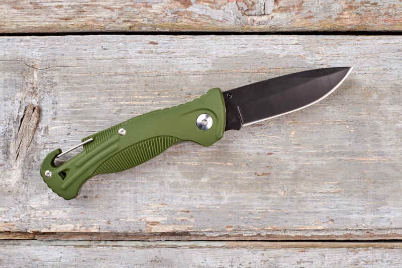 Army pocket knife with green handle. Wooden desk background.