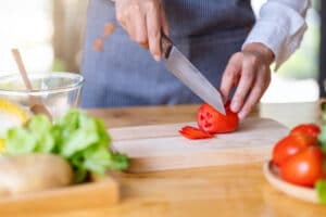 Closeup image of a chef cutting and chopping tomato by knife on wooden board