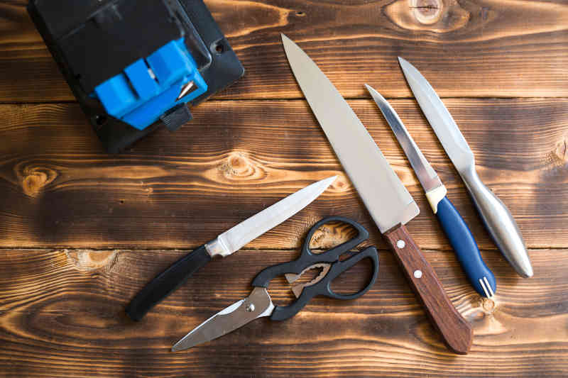 Layout of knives and scissors with a sharpening machine on a wooden table